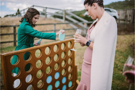 Image shows a bride and her friend playing Giant Connect 4 outside at her wedding